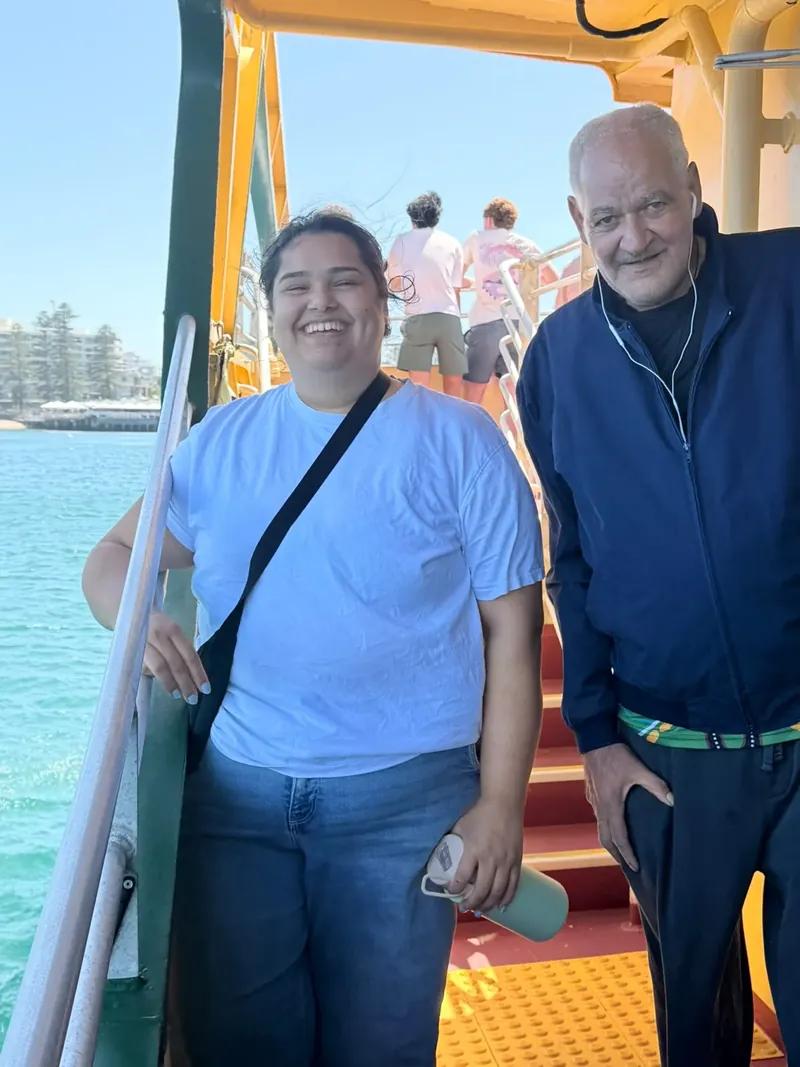 A support worker and participant smiling on the ferry steps on a harbour outing