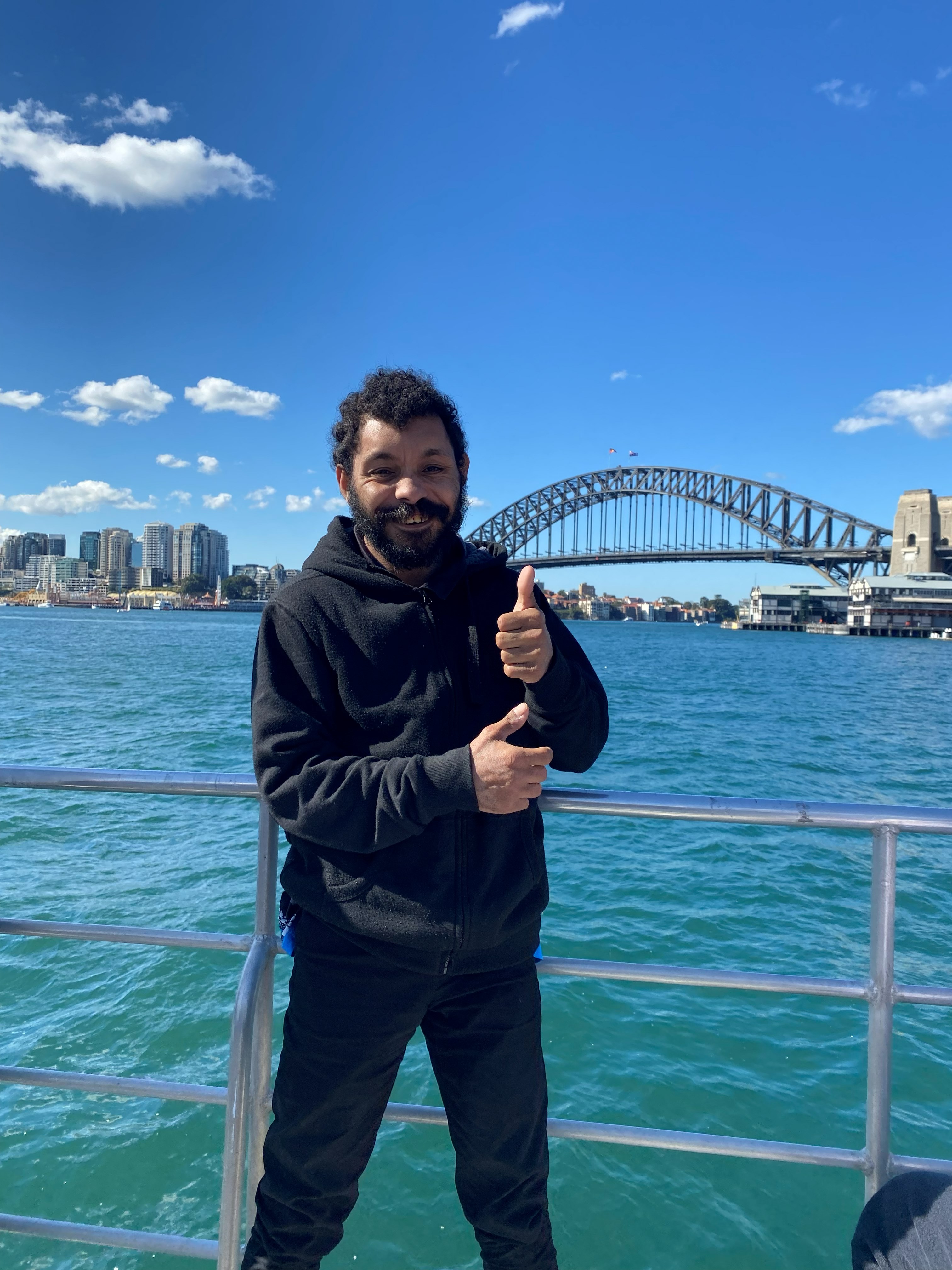 A participant giving a thumbs up on the ferry in front of the Harbour Bridge