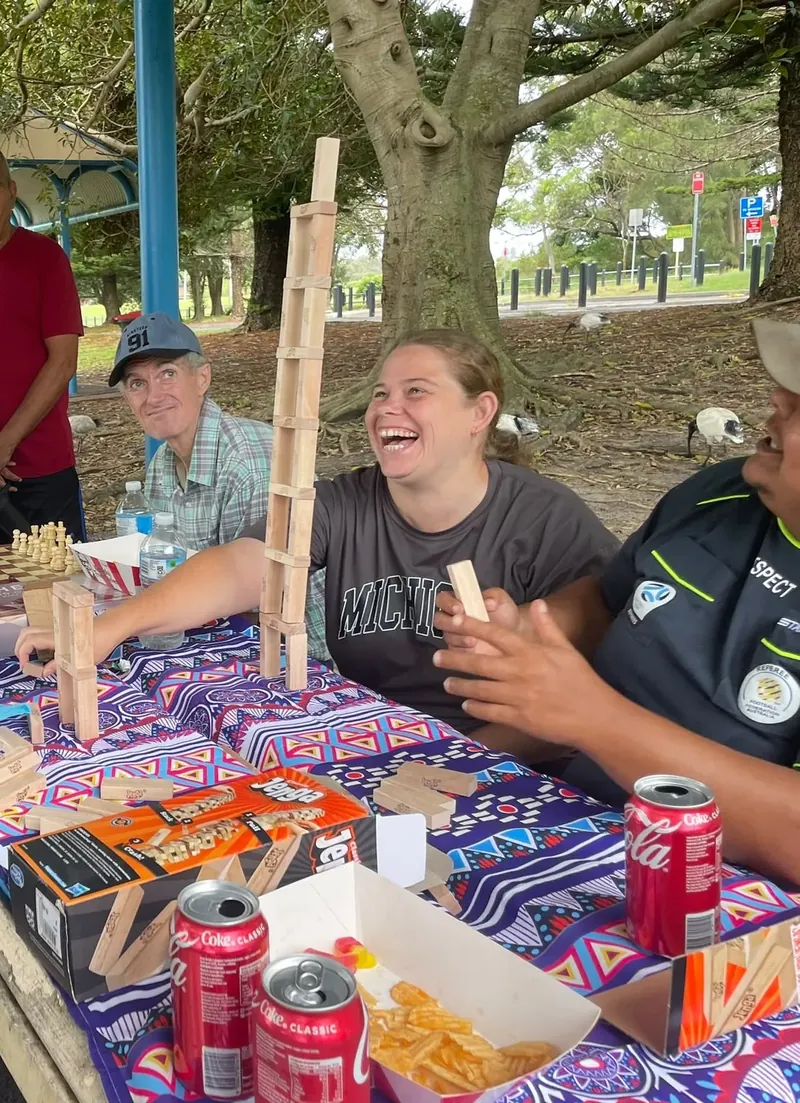 Participants laughing over a game of giant Jenga at a park picnic table
