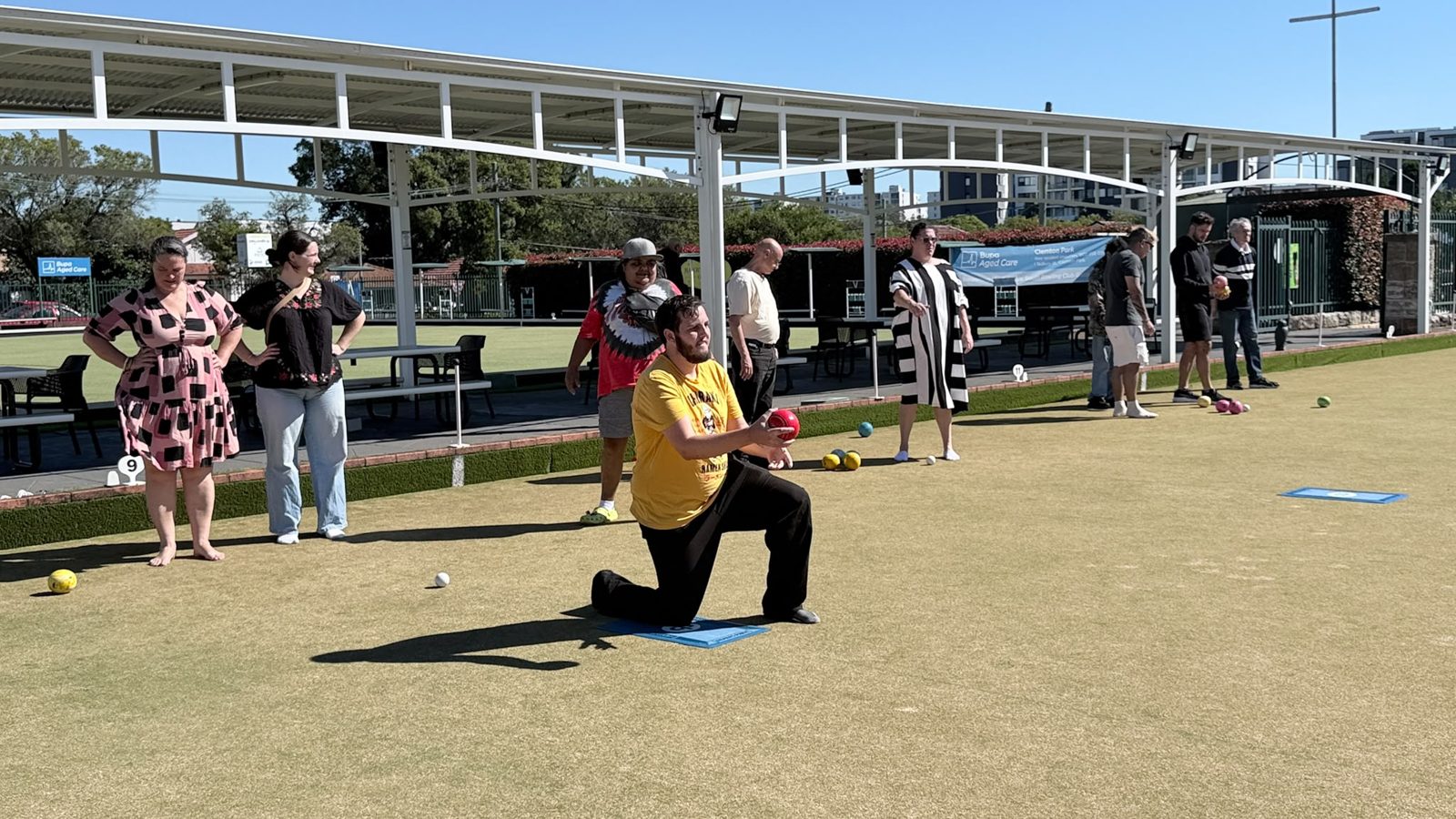 A participant playing lawn bowls on a sunny green during a community outing