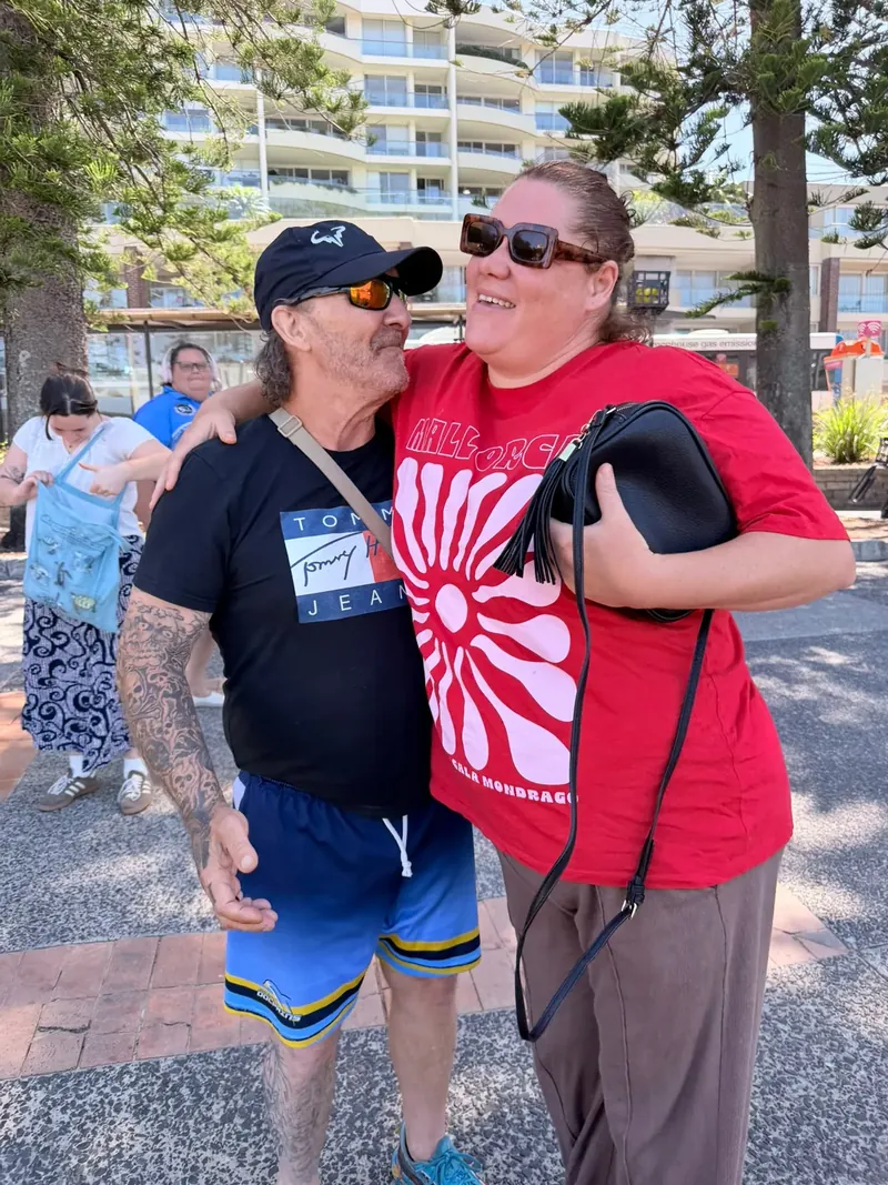 A participant and support worker sharing a laugh arm-in-arm at the beachfront