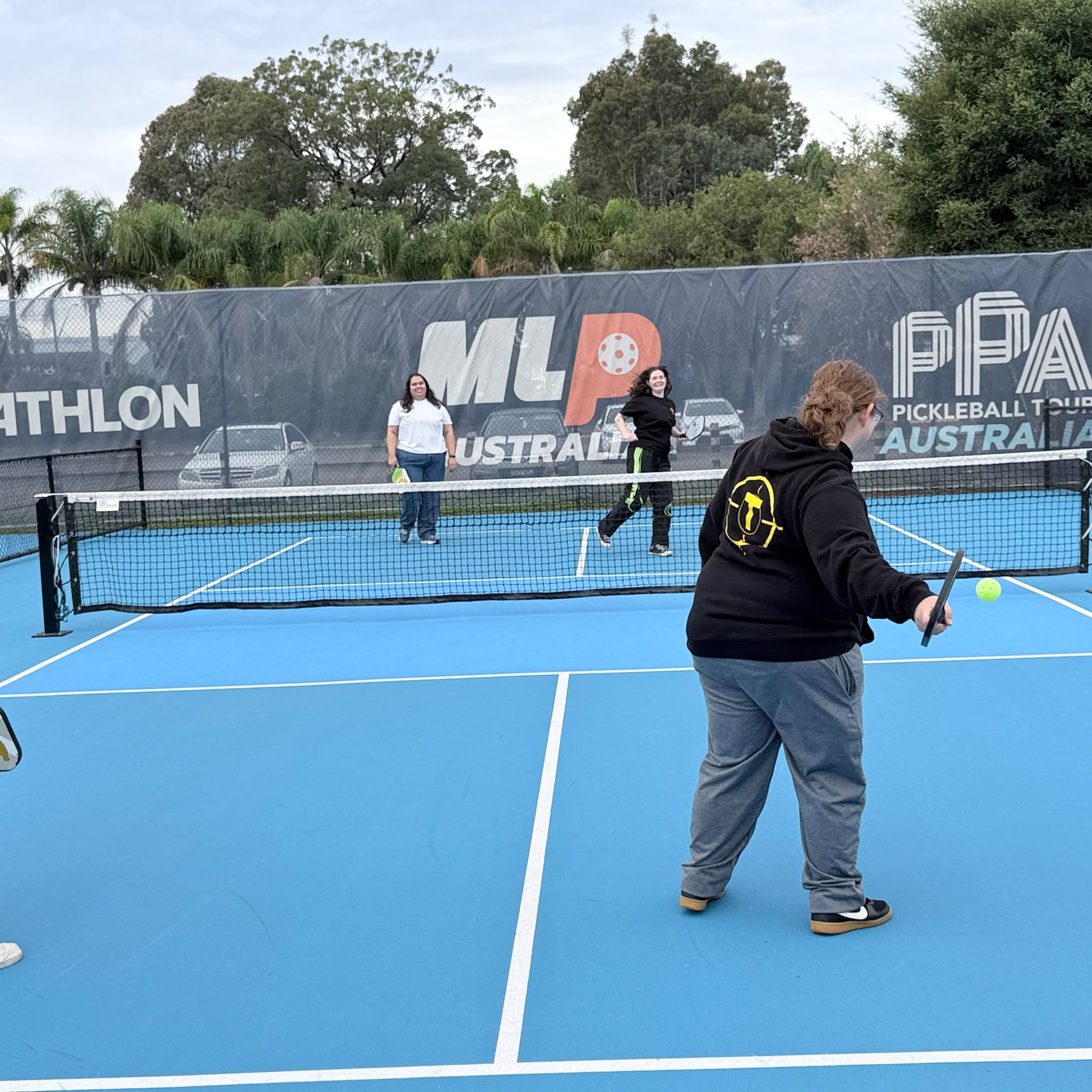 A Tegrity participant in a branded hoodie returning the ball during a pickleball rally at Pickle Point Sydney