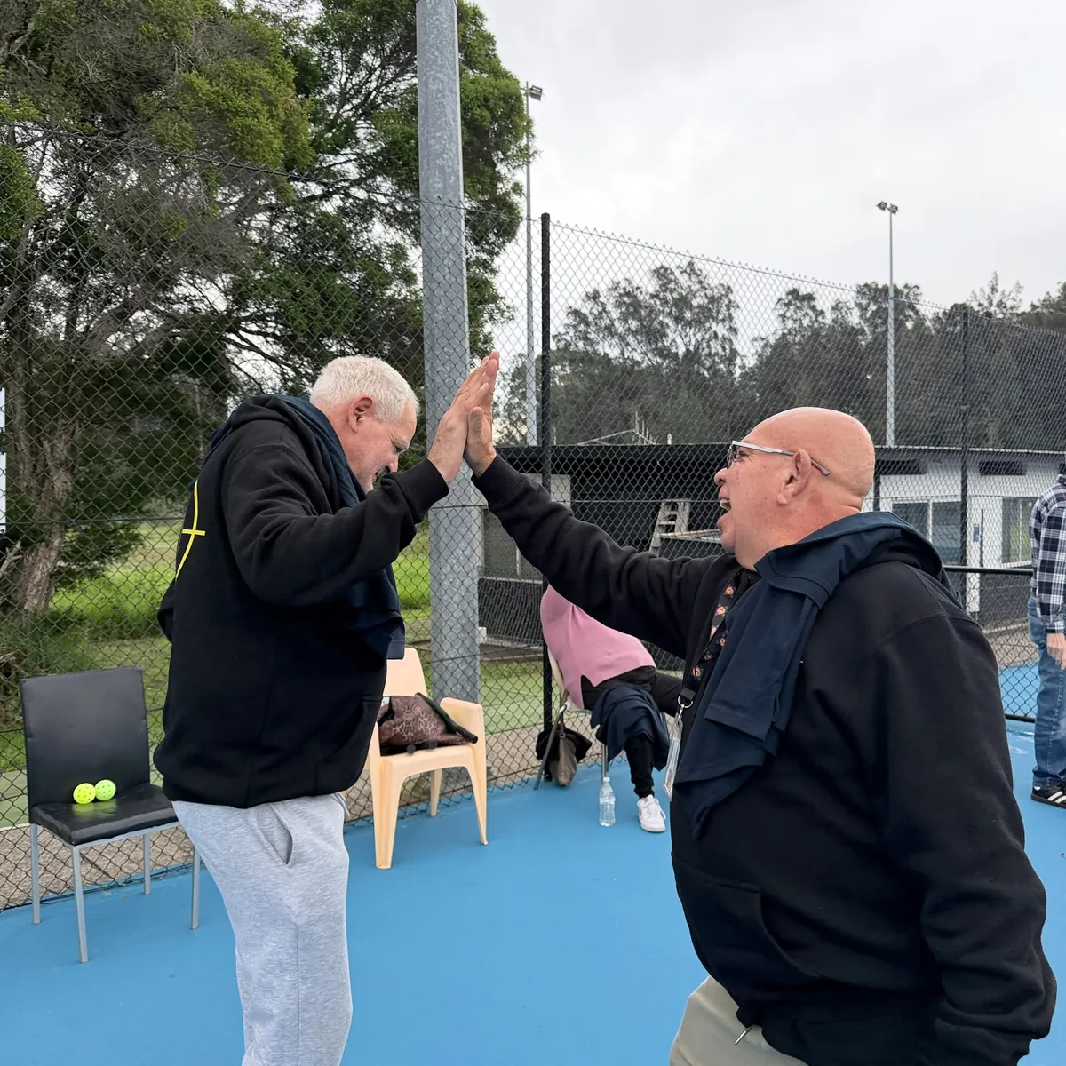 Two Tegrity participants high-fiving and laughing at the pickleball rec group day in Sydney