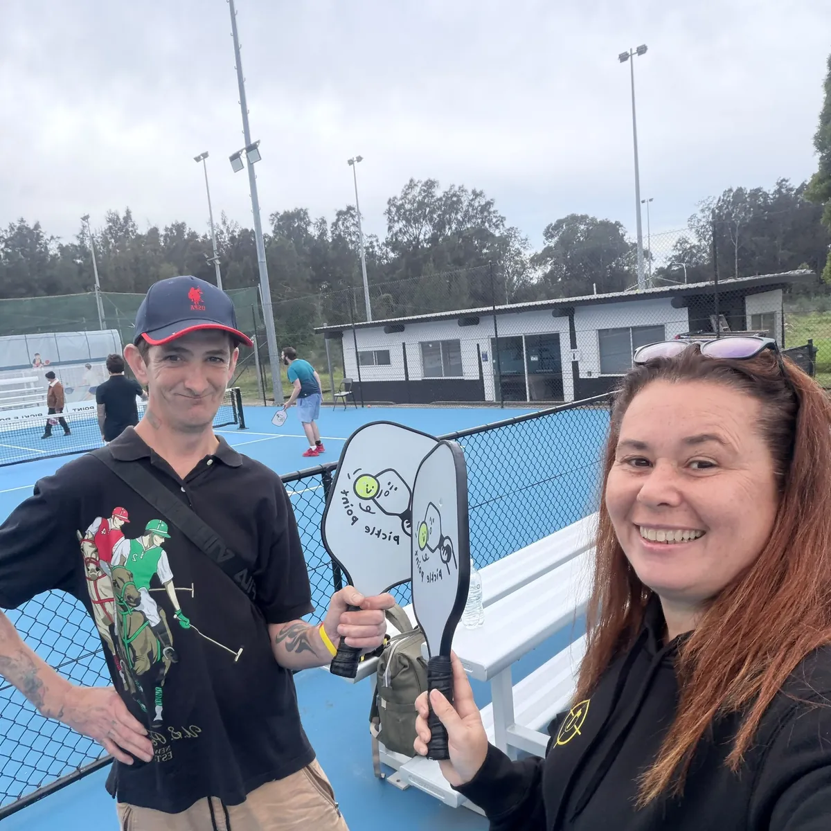 A Tegrity participant and support worker smiling with pickleball paddles at the courts
